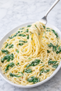Creamy lemon ricotta pasta with spinach on a large white oval platter on a marble counter with a fork twirling the noodles
