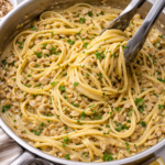 linguine tossed in garlicky white clam sauce in a skillet with silver tongs