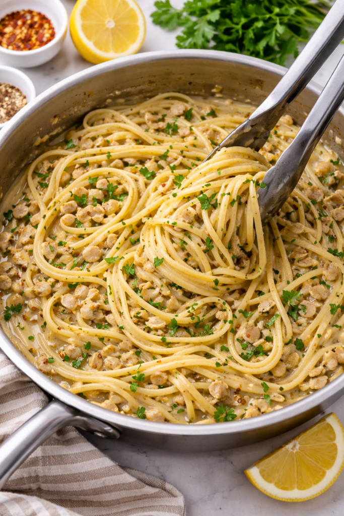 linguine tossed in garlicky white clam sauce in a skillet with silver tongs