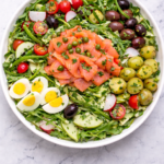 Lox Nicoise style salad with smoked salmon, potatoes, olives, green beans, tomatoes and eggs in a round white bowl