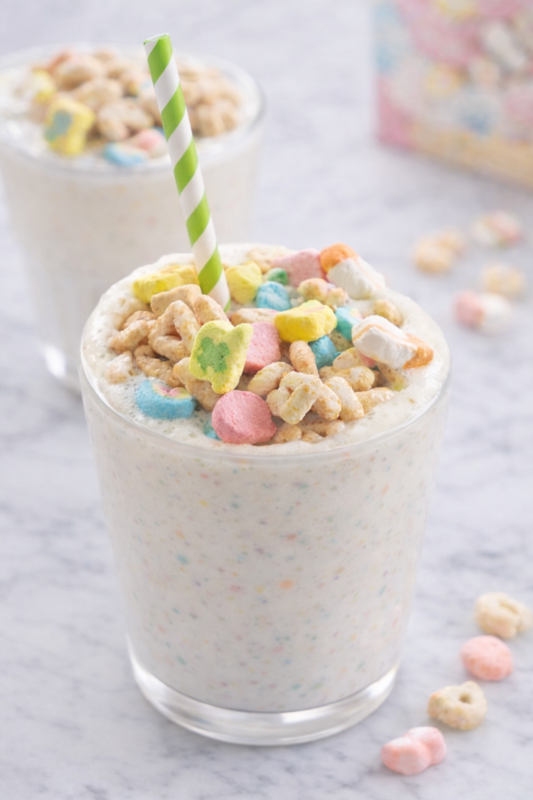 Lucky Charms milkshake with colorful marshmallow specks in a simple glass on a white marble countertop with green and white striped paper straw