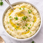 Creamy mashed celery potatoes in a white bowl with melted butter in the crevices, topped with parsley on a marble countertop