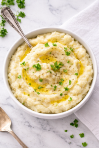 Creamy mashed celery potatoes in a white bowl with melted butter in the crevices, topped with parsley on a marble countertop