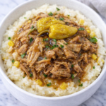 Mississippi pork roast mashed potato bowl with shredded pork, gravy, corn, and pepperoncini in a white bowl on marble counter