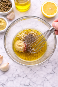 Whisking homemade Niçoise salad dressing with olive oil, Dijon mustard, garlic, lemon and vinegar in a glass bowl