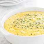 Old-fashioned corn pudding baked in a white casserole dish on a marble countertop, creamy Southern corn casserole topped with fresh chives