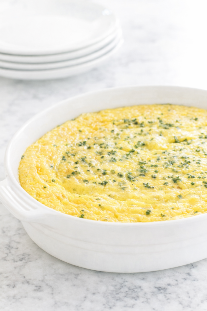 Old-fashioned corn pudding baked in a white casserole dish on a marble countertop, creamy Southern corn casserole topped with fresh chives
