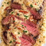 Pan seared ribeye steak sliced and topped with creamy Tuscan garlic parmesan sauce and sun dried tomatoes