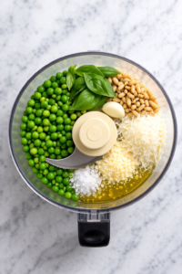 bird’s eye view of pea pesto ingredients in food processor before blending on marble counter