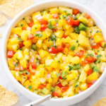 Bright pepper mango salsa in a white bowl on a marble counter with tortilla chips around it
