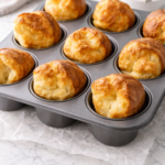 Golden homemade popovers baked in a popover pan on wrinkled parchment paper over a white marble countertop.