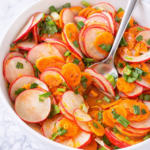 Radish carrot cilantro salad in a white bowl on a marble countertop with fresh citrus dressing