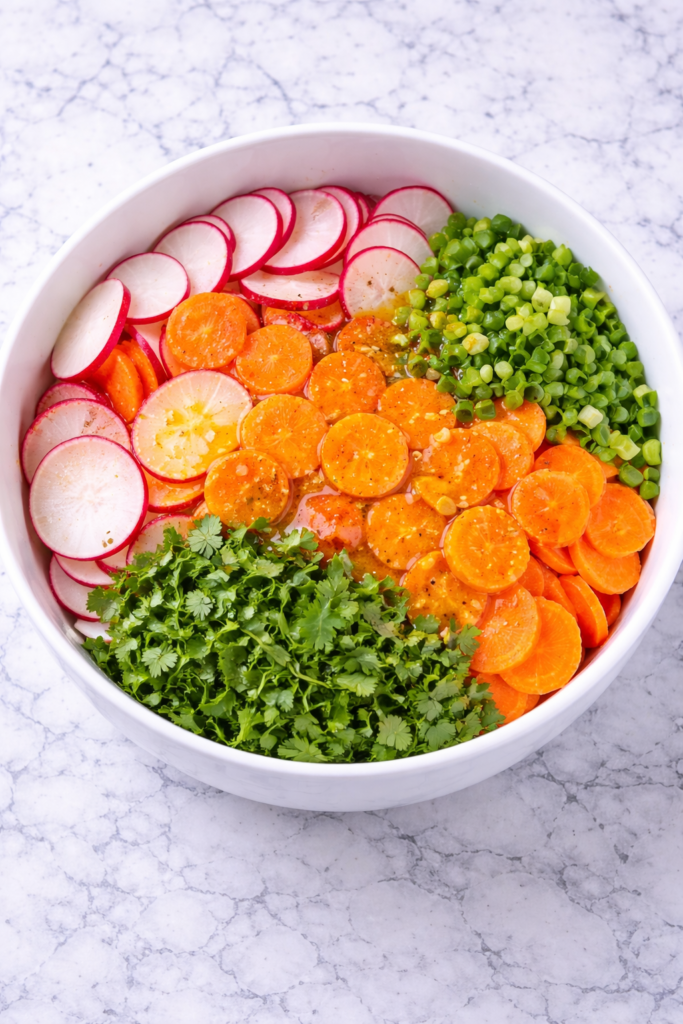 Radish carrot cilantro salad ingredients in a bowl before tossing on a marble countertop