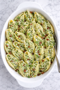 creamy ricotta pea pesto stuffed shells with bacon in white baking dish on marble counter