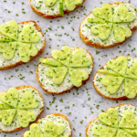 Shamrock crostinis made with cream cheese and cucumber shamrocks on toasted bread sprinkled with fresh chives on a marble counter