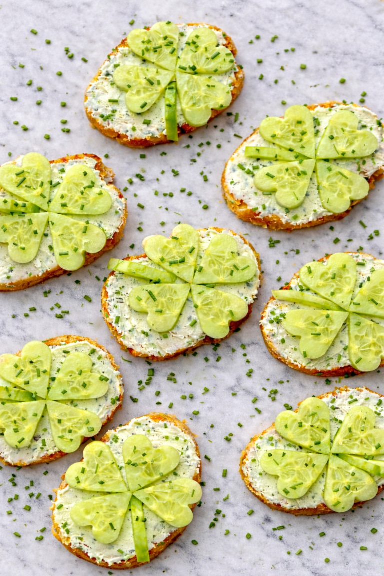 Shamrock crostinis made with cream cheese and cucumber shamrocks on toasted bread sprinkled with fresh chives on a marble counter