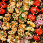 Sheet pan chicken souvlaki skewers with cherry tomatoes, zucchini, and red onion roasted on a well-loved baking sheet