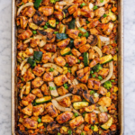 Sheet pan hibachi chicken with zucchini, onions, mushrooms and carrots roasted on a well used baking sheet on a marble counter