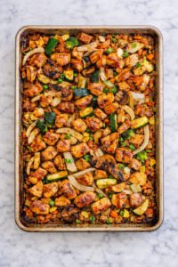 Sheet pan hibachi chicken with zucchini, onions, mushrooms and carrots roasted on a well used baking sheet on a marble counter