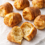 Simple homemade popovers on wrinkled parchment paper with one popover split open showing the airy inside on a white marble counter