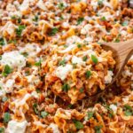 Skillet lasagna with Mediterranean meat sauce, cottage cheese, cinnamon, and mint being scooped with a wooden spoon from a silver skillet