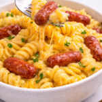 Creamy cheddar rotini pasta with cocktail weenies in a bowl with a fork lifting a cheesy bite