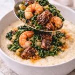 Spoon adding cooked shrimp, sausage, and kale mixture over creamy fontina cheese grits in a neutral bowl.