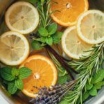 Overhead view of spring stovetop potpourri with lemon, orange slices, rosemary, mint, lavender, and vanilla bean in a pot