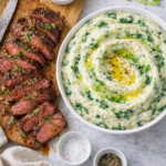 Sliced juicy steak on a cutting board next to creamy Irish colcannon with kale and Boursin cheese in a white bowl