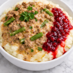 Swedish meatball mashed potato bowl with creamy ground beef gravy, green beans, and lingonberry jam on white marble counter