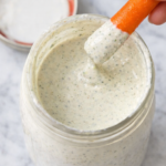 Carrot stick dipping into homemade Sweet Tomatoes homestyle ranch dressing in a glass jar on a marble countertop