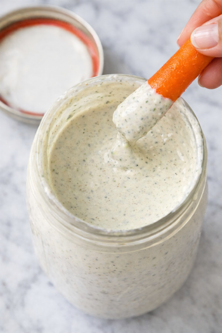Carrot stick dipping into homemade Sweet Tomatoes homestyle ranch dressing in a glass jar on a marble countertop
