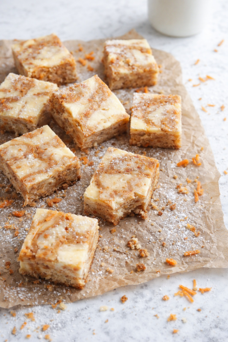Swirled carrot cake cheesecake bars on wrinkled brown parchment paper with powdered sugar, shredded carrots, crumbs, and a bite taken out, styled on a marble countertop