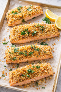 Walnut rosemary crusted salmon fillets baked on a parchment lined sheet pan with lemon wedges