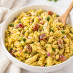 creamy chicken curry pasta salad with chicken pieces grapes celery and herbs in a white bowl on a marble countertop