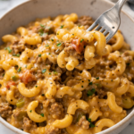 Close-up of creamy slow cooker hamburger helper with ground beef and elbow pasta in a bowl with a fork lifting a cheesy bite