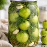Jar of whole Jersey dill pickled green tomatoes with garlic and fresh dill on a marble countertop