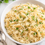Fluffy homemade rice pilaf with toasted orzo and fresh parsley in a white bowl on a marble counter with a spoon and neutral cloth