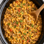 Slow cooker hamburger helper with ground beef, elbow pasta, and creamy cheesy sauce in a black crockpot on a marble counter with a wooden spoon