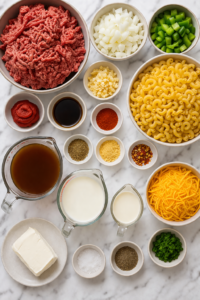 Flat lay of ingredients for slow cooker hamburger helper including ground beef, elbow macaroni, cheese, broth, milk, cream, onion, bell pepper, garlic, and seasonings on a marble counter