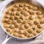 Swedish meatballs simmering in creamy gravy in a stainless steel skillet on a marble countertop
