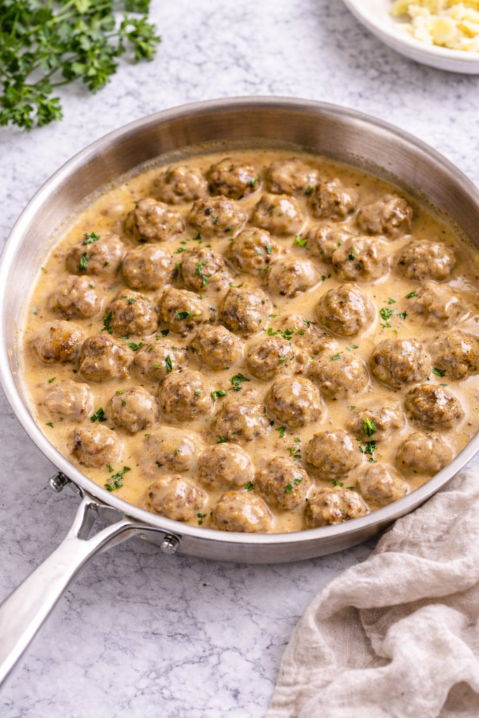 Swedish meatballs simmering in creamy gravy in a stainless steel skillet on a marble countertop