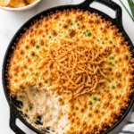 Creamy baked Bloomin’ Onion Dip topped with crispy fried onions in a cast iron skillet on a white marble countertop