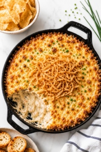 Creamy baked Bloomin’ Onion Dip topped with crispy fried onions in a cast iron skillet on a white marble countertop