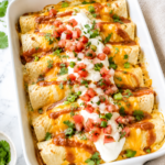 White baking dish filled with cheesy breakfast enchiladas topped with taco sauce, sour cream, pico de gallo, and fresh cilantro on a marble countertop.