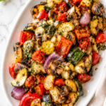 Grilled ratatouille salad with zucchini, squash, mushrooms, peppers, onions, and tomatoes on a white platter over a marble countertop