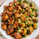 Kung pao chicken and roasted Brussels sprouts plated in a white bowl with peanuts and green onions on a marble countertop