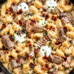 Creamy one pan loaded steak and gnocchi skillet topped with crispy bacon, sour cream, and fresh chives in a cast iron skillet