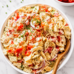 Creamy Southern cracker salad with tomatoes and red onion in a white bowl with a wooden spoon on a white marble countertop