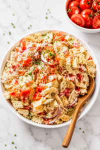 Creamy Southern cracker salad with tomatoes and red onion in a white bowl with a wooden spoon on a white marble countertop